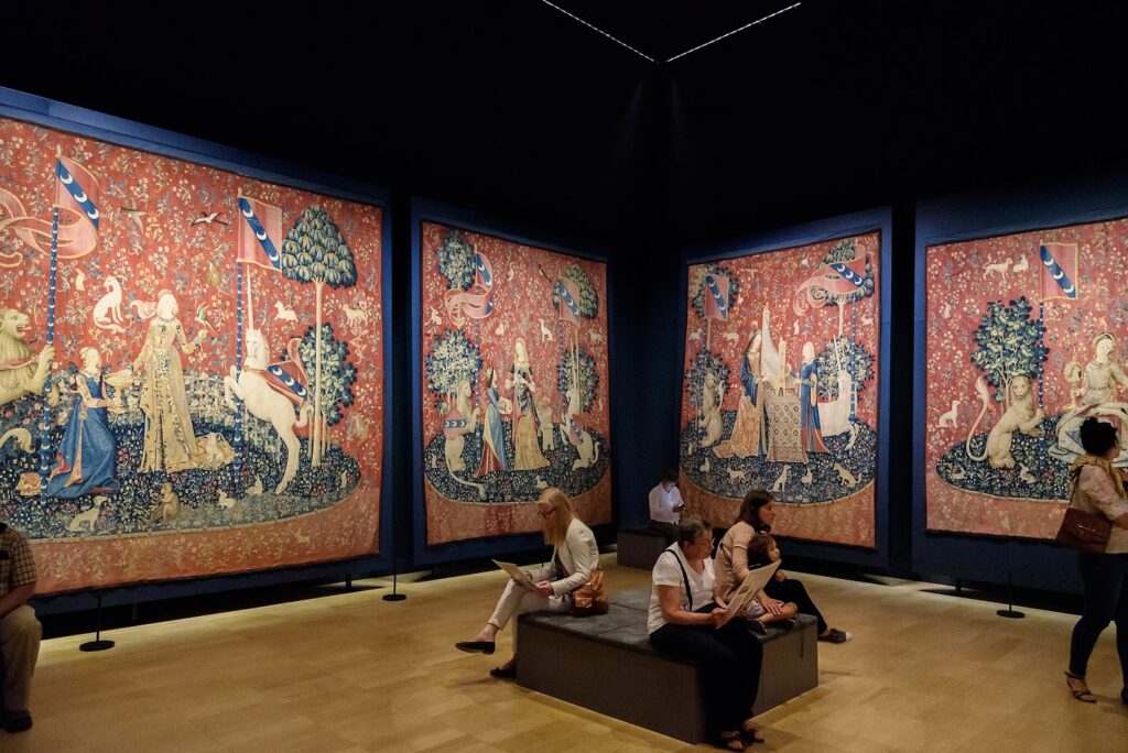 This image depicts the gallery at the Musée de Cluny where the Lady and the Unicorn tapestry series are displayed. It is included to give the reader visual perspective on how large the tapestries are.